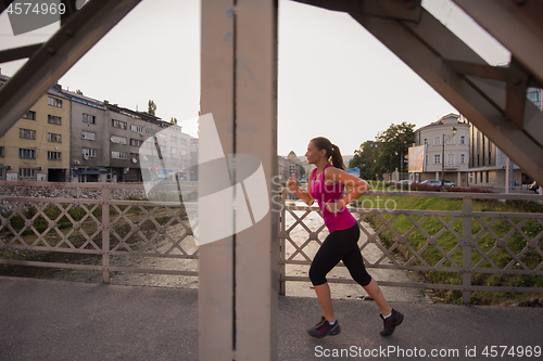 Image of woman jogging across the bridge at sunny morning