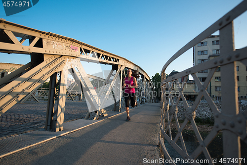 Image of woman jogging across the bridge at sunny morning