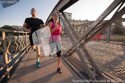 Image of young couple jogging across the bridge in the city