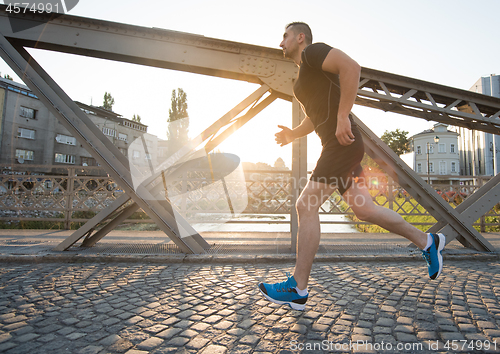 Image of man jogging across the bridge at sunny morning