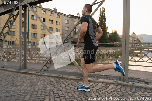 Image of man jogging across the bridge at sunny morning