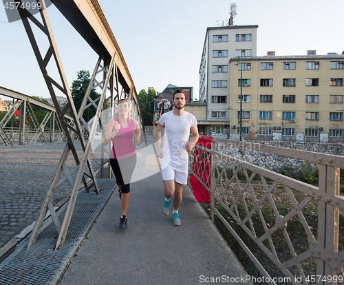 Image of young couple jogging across the bridge in the city