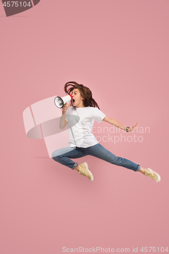 Image of Beautiful young woman jumping with megaphone isolated over pink background