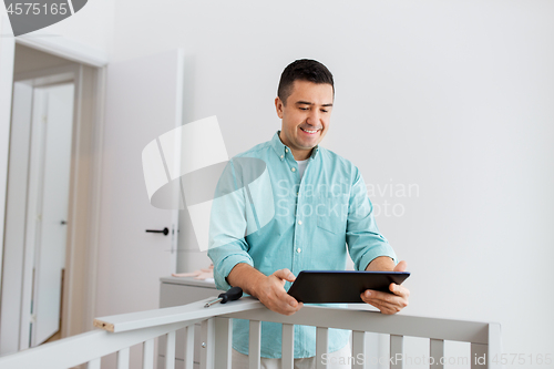 Image of father with tablet pc assembling baby bed at home