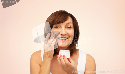 Image of smiling senior woman applying cream to her face