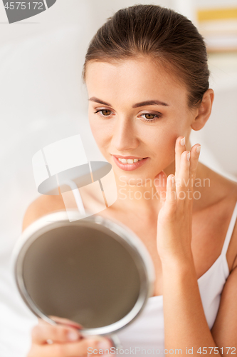 Image of beautiful woman looking to mirror touches her face