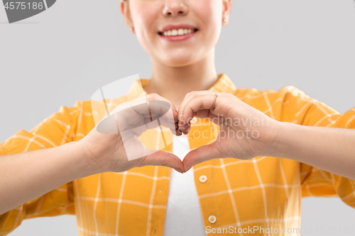 Image of smiling teenage girl making heart gesture