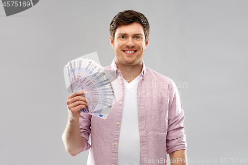 Image of smiling young man with fan of euro money over grey