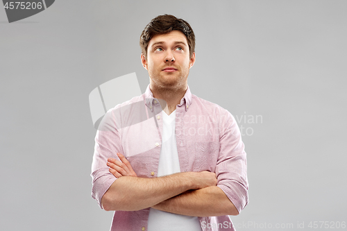 Image of suspecting young man with crossed hands looking up