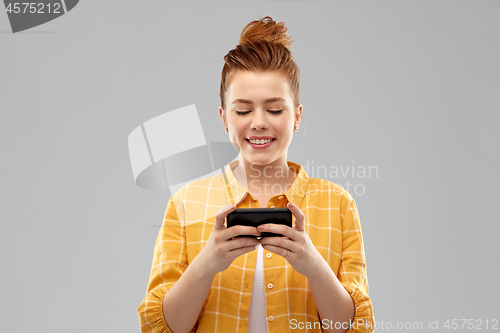 Image of smiling red haired teenage girl using smartphone