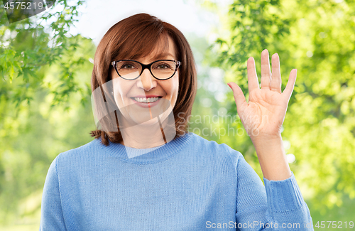 Image of portrait of senior woman in glasses waving hand