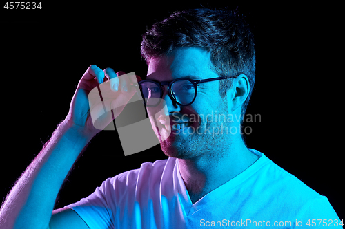 Image of man in glasses over neon lights in dark room