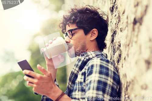 Image of man with smartphone drinking coffee on city street