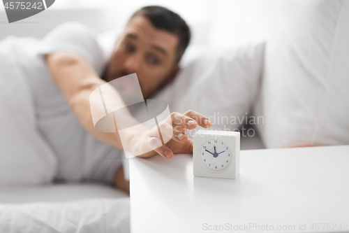 Image of close up of man in bed reaching for alarm clock