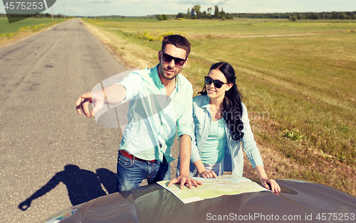 Image of happy man and woman with road map on car hood