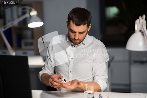 Image of businessman taking medicine pills at night office