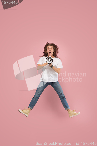 Image of Beautiful young woman jumping with megaphone isolated over pink background