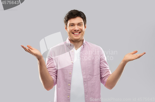 Image of happy young man shrugging over grey background