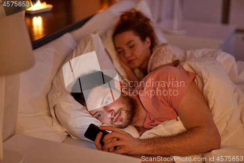 Image of man using smartphone while girlfriend is sleeping