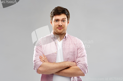 Image of indifferent young man with crossed hands over grey