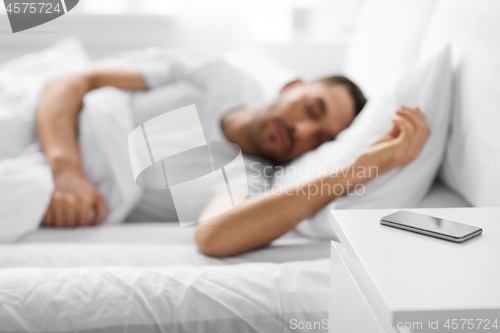 Image of smartphone on bedside table near sleeping man