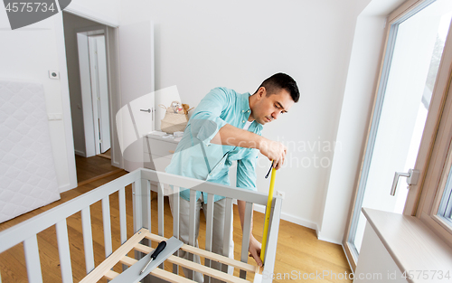 Image of father with tablet pc and ruler measuring baby bed