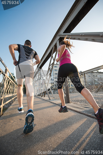 Image of young couple jogging across the bridge in the city