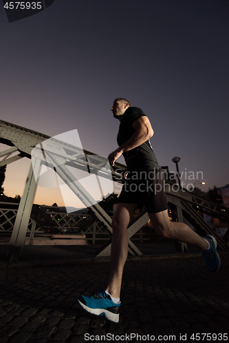 Image of man jogging across the bridge in the city