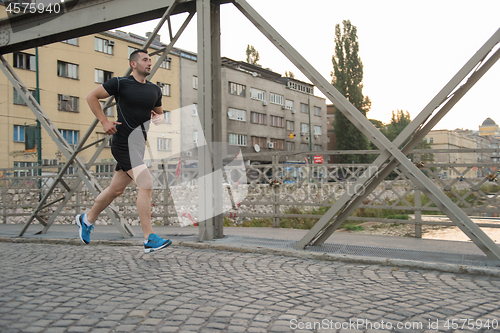 Image of man jogging across the bridge at sunny morning