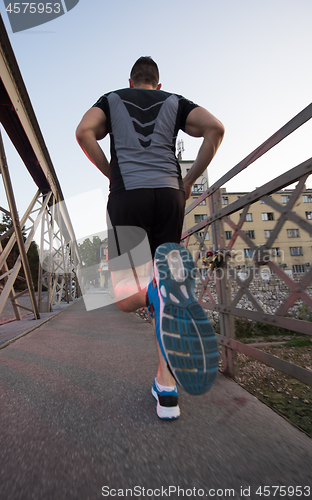 Image of man jogging across the bridge at sunny morning