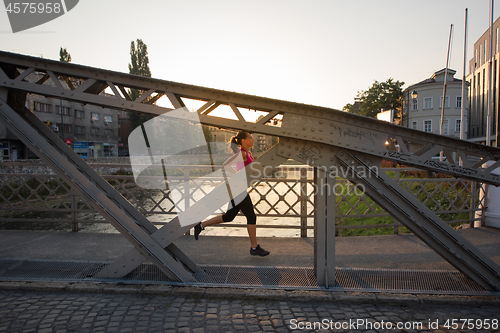 Image of woman jogging across the bridge at sunny morning