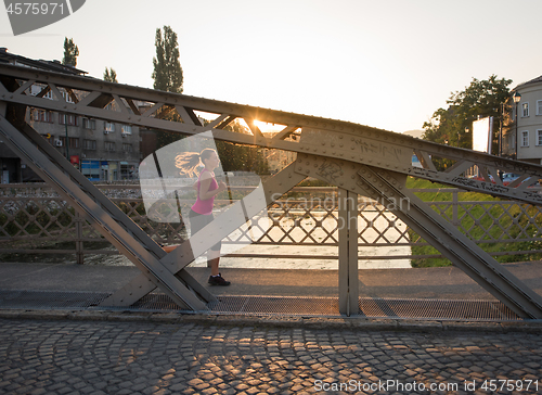 Image of woman jogging across the bridge at sunny morning