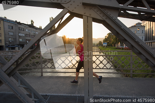 Image of woman jogging across the bridge at sunny morning