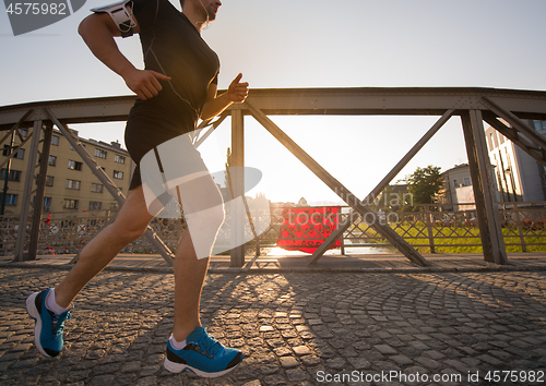 Image of man jogging across the bridge at sunny morning