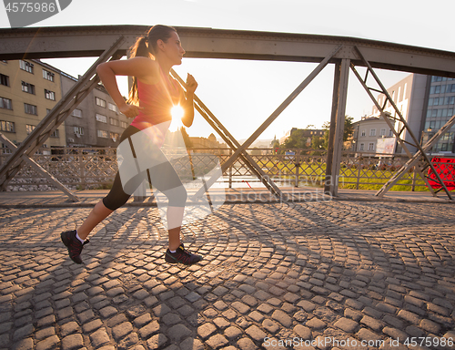 Image of woman jogging across the bridge at sunny morning