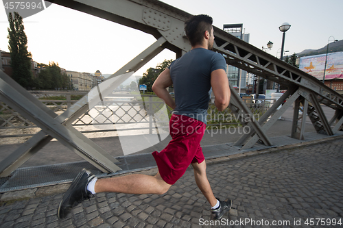 Image of man jogging across the bridge at sunny morning