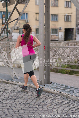 Image of woman jogging across the bridge at sunny morning