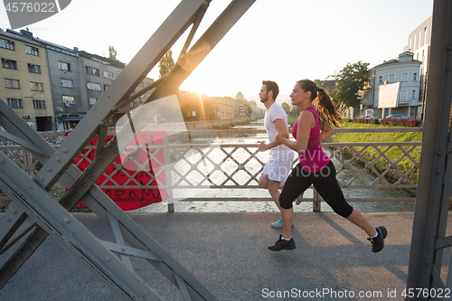 Image of young couple jogging across the bridge in the city