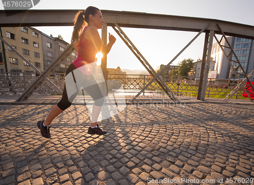 Image of woman jogging across the bridge at sunny morning