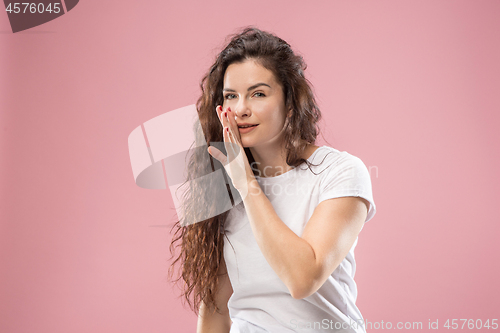 Image of The young woman whispering a secret behind her hand over pink background