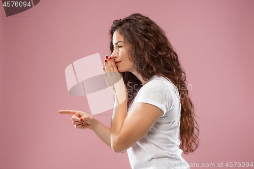 Image of The young woman whispering a secret behind her hand over pink background