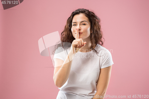 Image of The young woman whispering a secret behind her hand over pink background