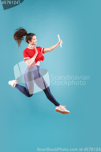 Image of Image of young woman over pink background using laptop computer or tablet gadget while jumping.