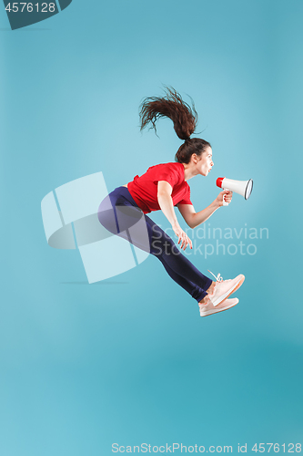 Image of Beautiful young woman jumping with megaphone isolated over red background