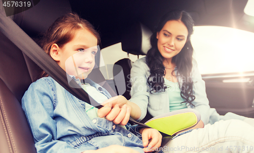 Image of happy woman fastening child with seat belt in car