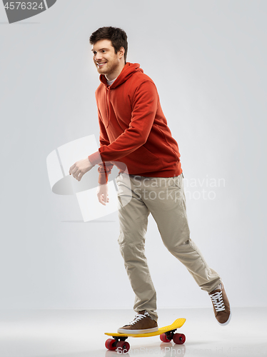 Image of smiling young man in hoodie riding on skateboard