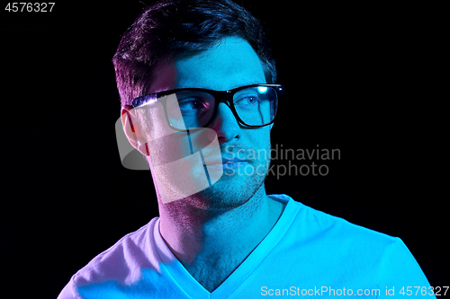 Image of man in glasses over neon lights in dark room