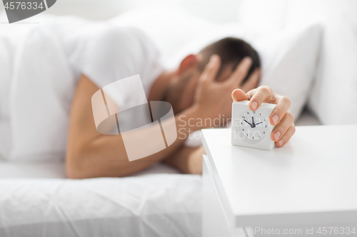 Image of close up of man in bed reaching for alarm clock