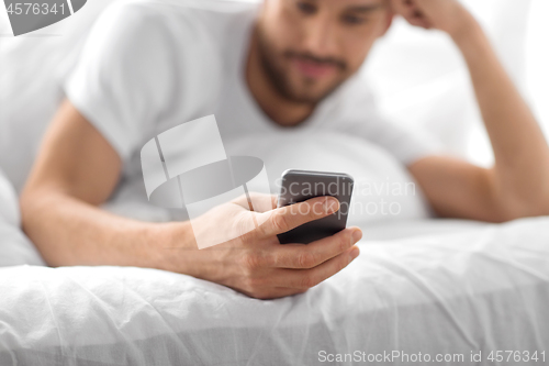 Image of close up of man with smartphone in bed in morning