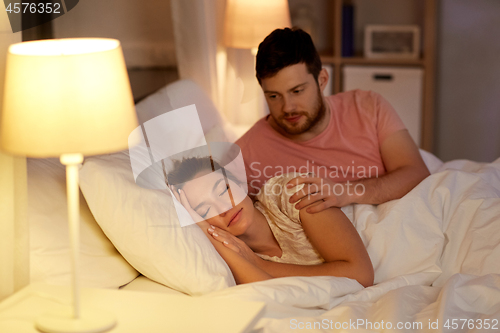 Image of man waking his sleeping wife up in bed at home